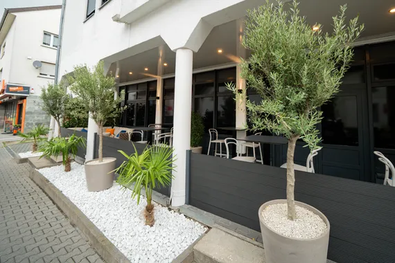 Außenbereich des Restaurant AURO Langen mit Terrasse und Olivenbäumen