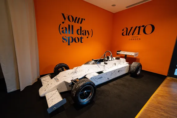 Rennwagen als Deko-Highlight vor der orangefarbenen „your (all day) spot“-Wand im AURO Langen