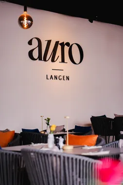 AURO-Logo an der weißen Wand über gedeckten Tischen im Restaurant AURO Langen