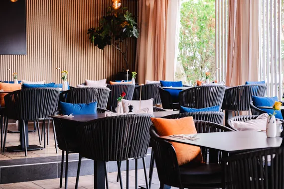 Gedeckte Tische mit Rattanstühlen und farbigen Kissen am Fenster im Restaurant AURO Langen