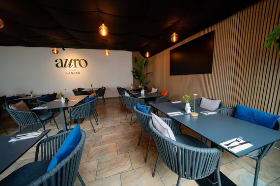 Gastraum mit Holzlamellenwand, dunklen Tischen und blauen Stühlen im Restaurant AURO Langen