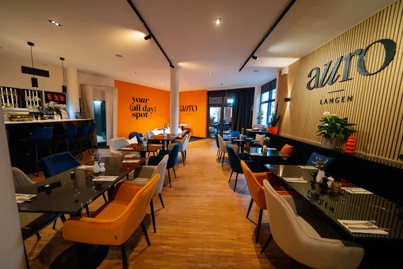 Blick über den hellen Gastraum mit Bar und orangefarbenen Sesseln im Restaurant AURO Langen