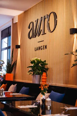 Holzlamellenwand mit AURO-Logo und gemütlicher Sitzbank im Restaurant AURO Langen